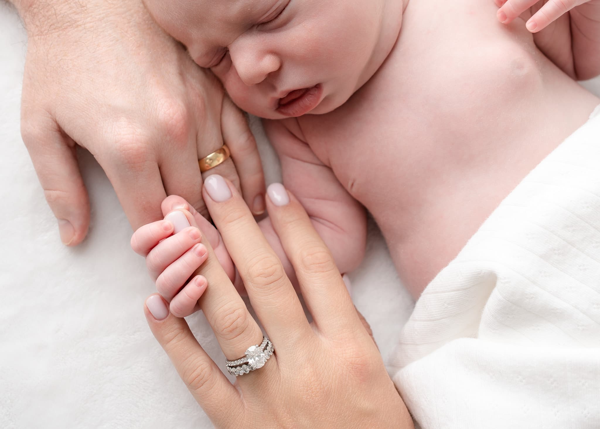 A newborn's hand curled around a parent's finger, both parents' hands resting beside them